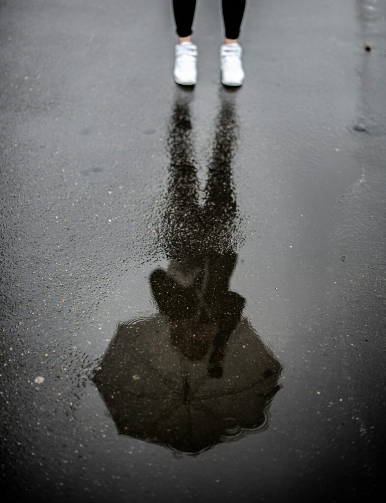 Person's reflection seen in a rain puddle